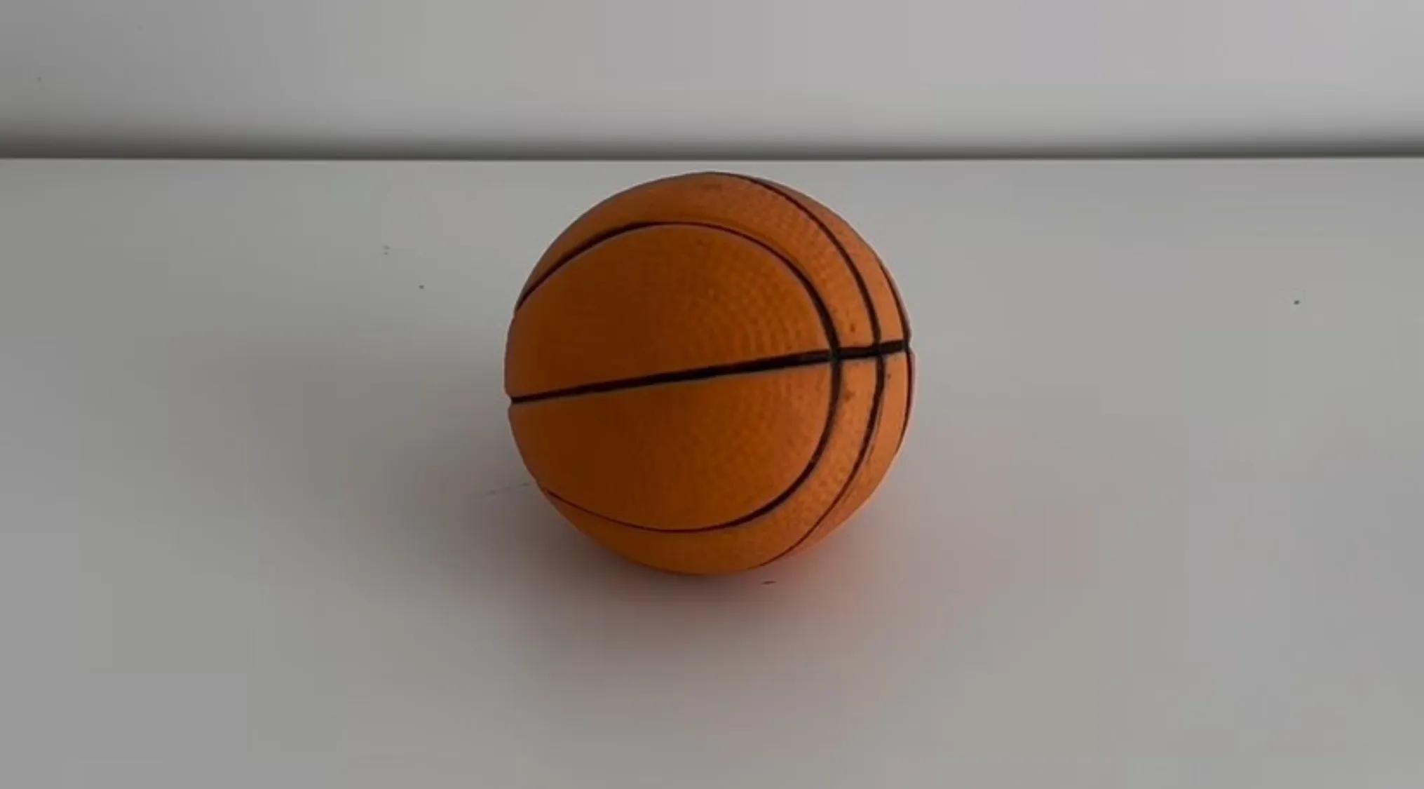 Orange basketball with black lines on a white surface, raising questions if it is real, cake, or slime.