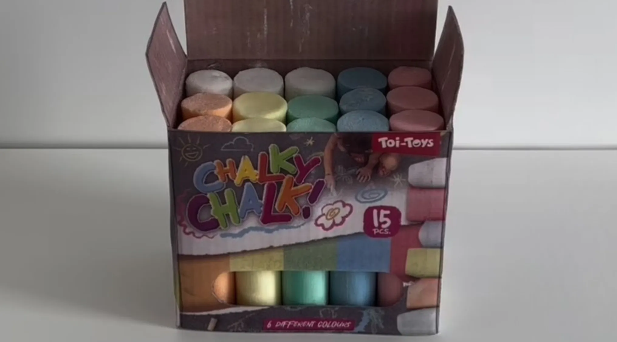 Box of colorful chalk sticks neatly arranged in an open cardboard package with playful branding and 15 pieces inside.