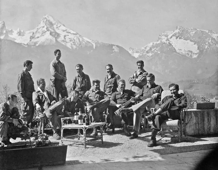 Group of men in military uniforms gathered outdoors with mountains in the background, a historic site photo capturing history repeated.