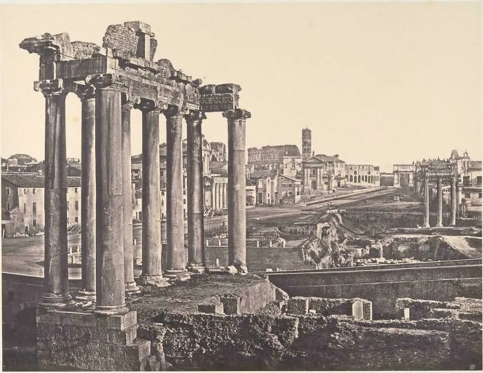 Ancient historic site ruins with tall stone columns and surrounding old buildings under a clear sky.
