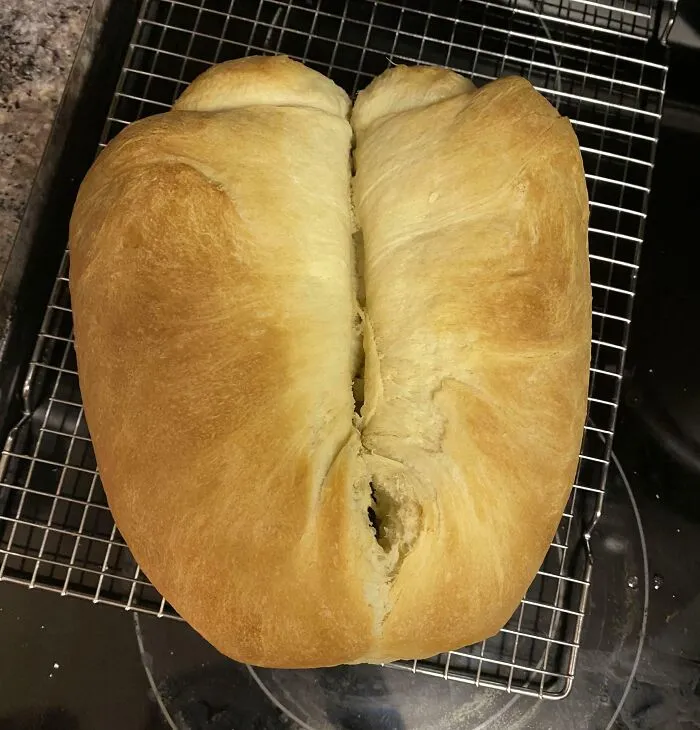 Overbaked dessert loaf with uneven shape and cracked center sitting on cooling rack after ruining dessert attempt.
