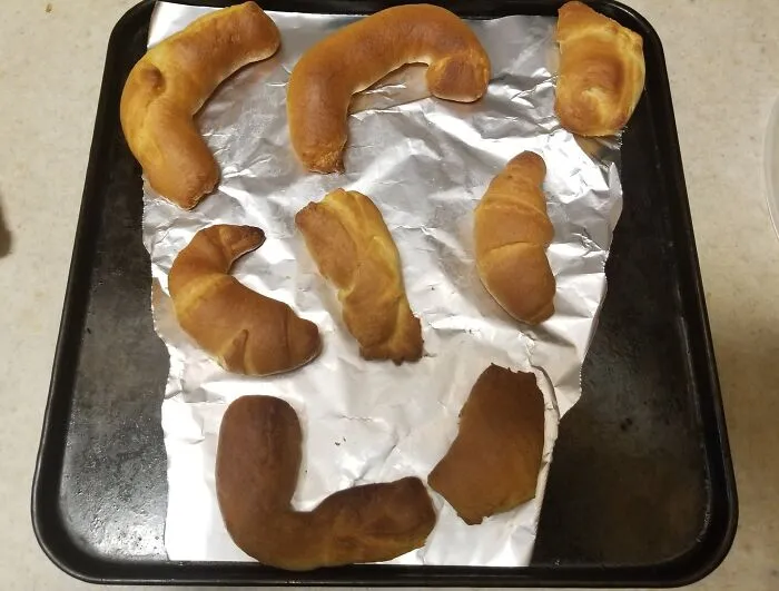 Croissants on a baking sheet with foil, showing uneven baking and misshapen forms ruining the dessert appearance.