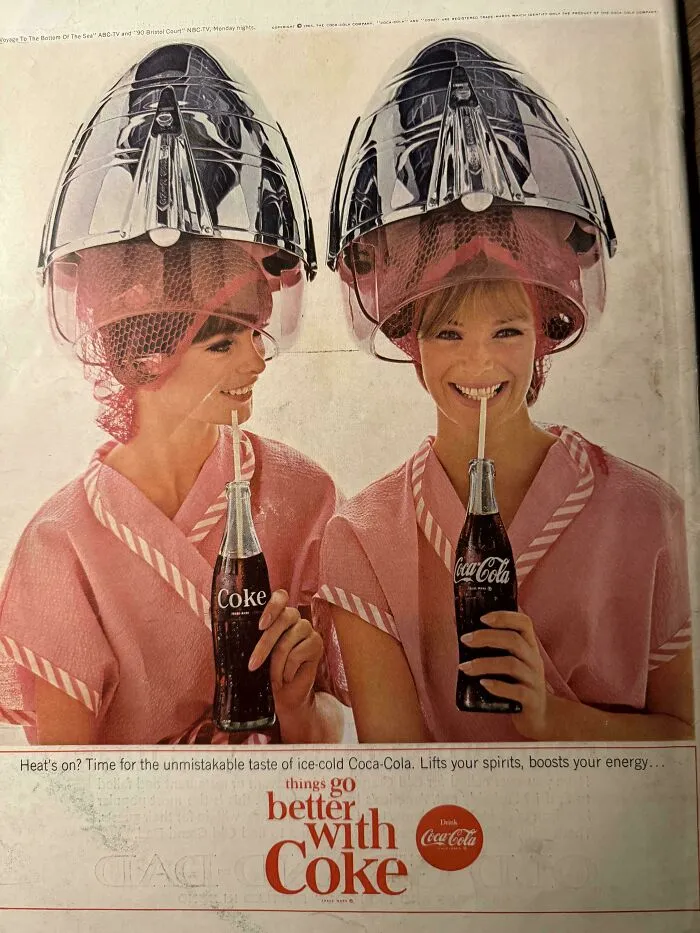 Vintage women’s ad showing two women under hair dryers drinking ice-cold Coke, reflecting different societal norms in the past.