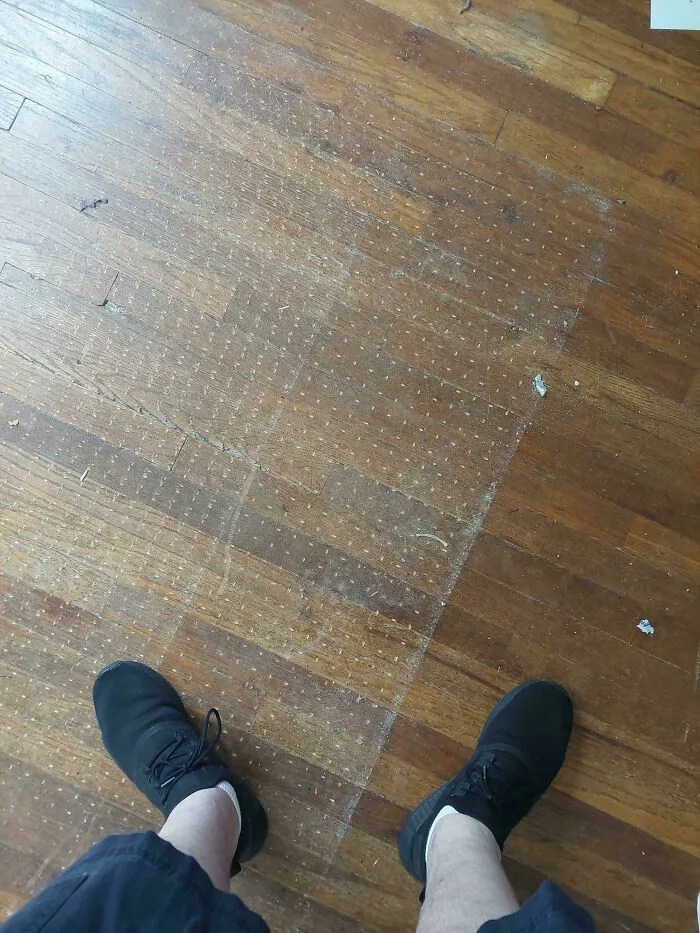 Worn shoes revealing a cleaner floor patch, an unfortunate event captured on a wooden surface.