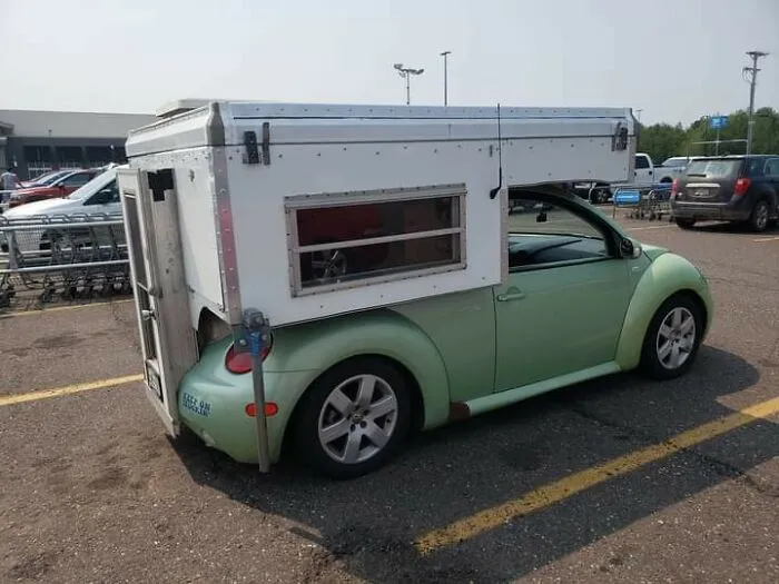A green car with a custom-built camper shell attached, illustrating if it's stupid but it works concept.