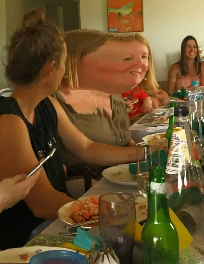 Group of people at a dinner table with distorted faces caused by a panoramic photo fail capturing a humorous moment.