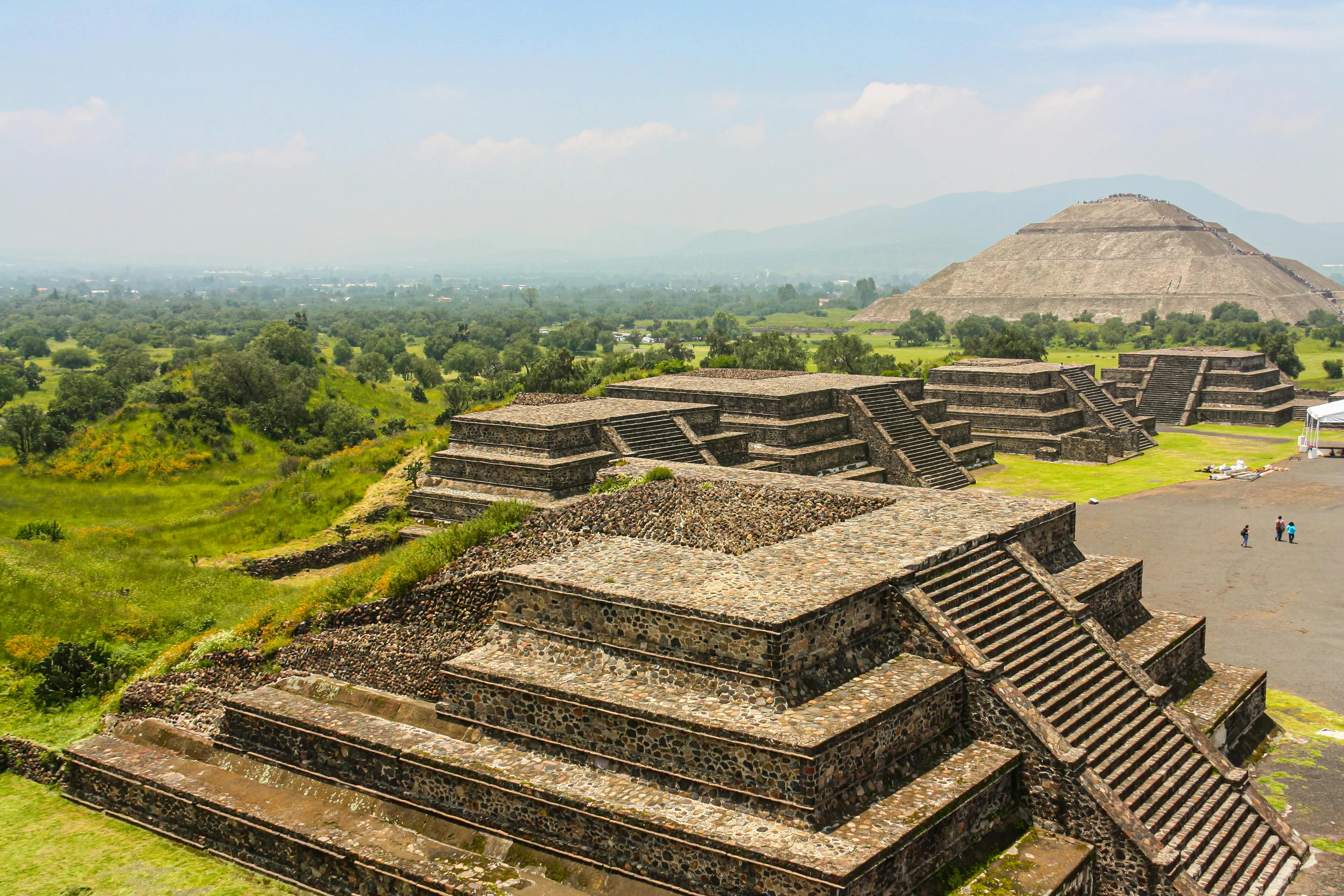Stone pyramids and ruins at an ancient archaeological site representing the Aztec Empire in a lush green landscape.