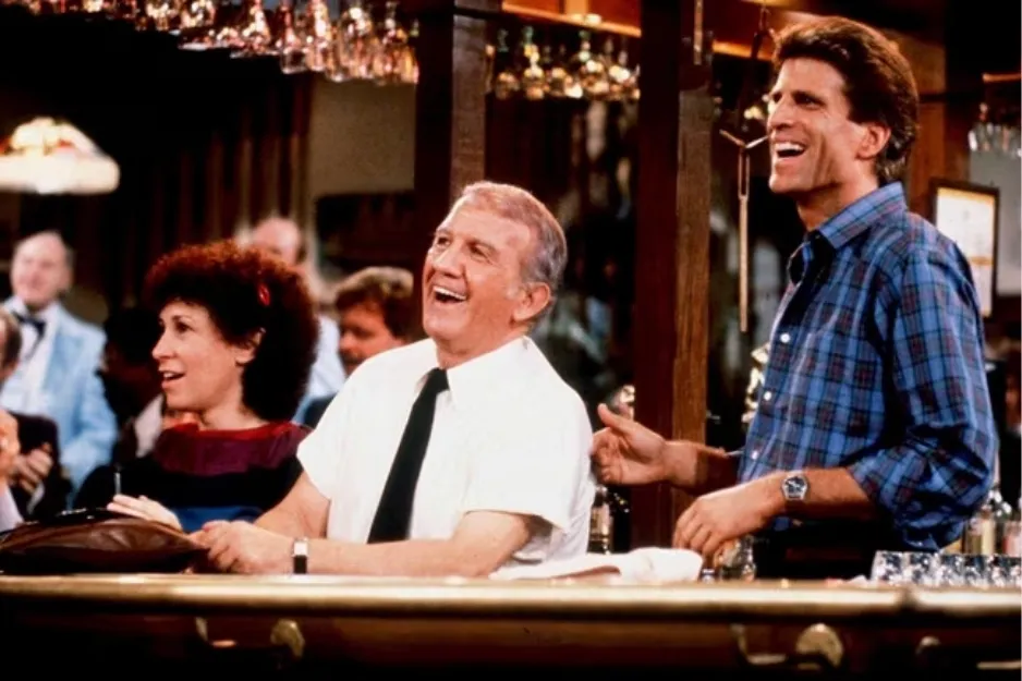Characters laughing and socializing in a bar setting from the sitcom Cheers at MacLaren’s bar.