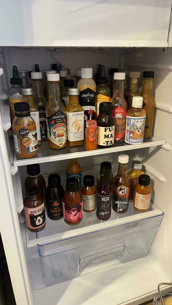 Open fridge filled with an assortment of hot sauce bottles showing a fridge collection for spicy condiments enthusiasts.