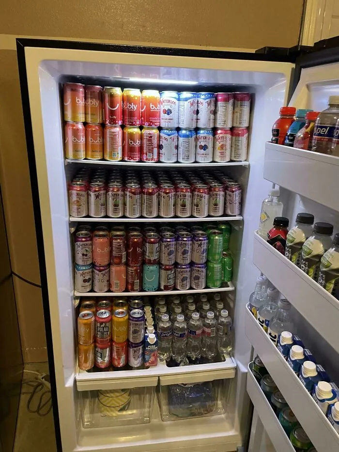 Open fridge fully stocked with various drinks neatly arranged on shelves and door compartments in a well-lit interior.