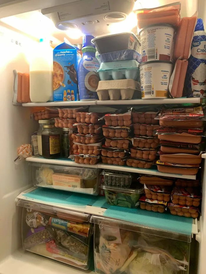 Fridge packed with dozens of hot dog packs, dairy products, and condiments stacked on multiple shelves.