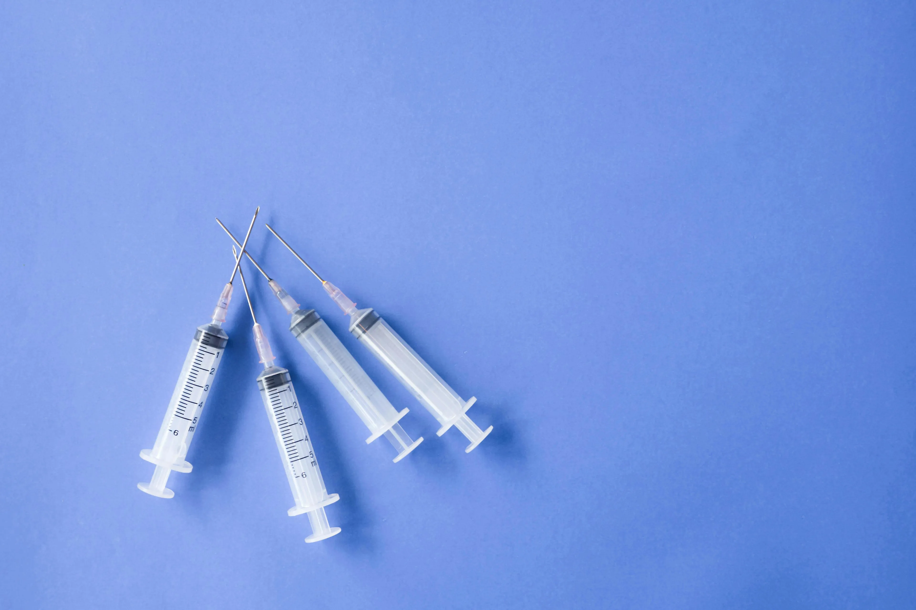 Four empty syringes with needles on a blue background illustrating compression of air and temperature change in science.
