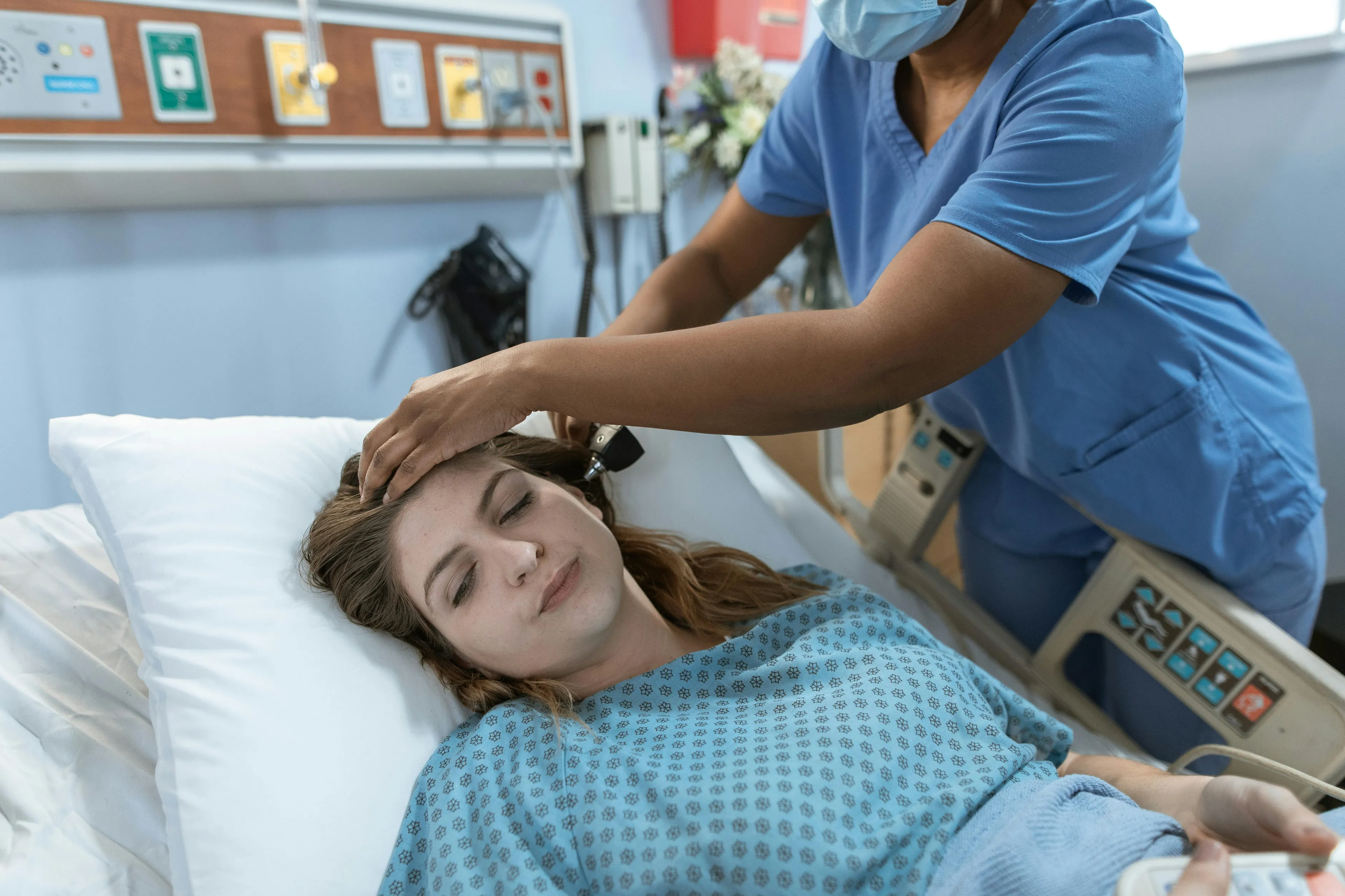 Nurse in blue scrubs examining patient in hospital bed related to thyroid gland and body system malfunction.