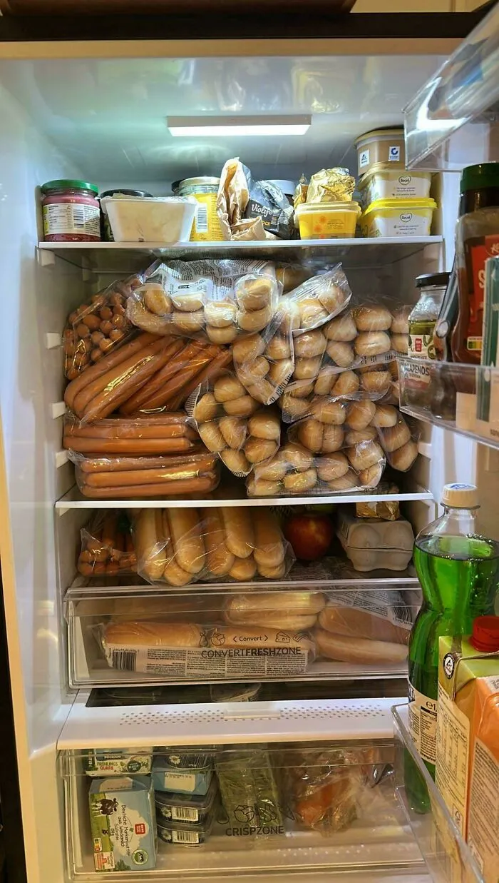 Open fridge stuffed with numerous packaged hot dogs and buns, illustrating horrifying fridge finds shared online.
