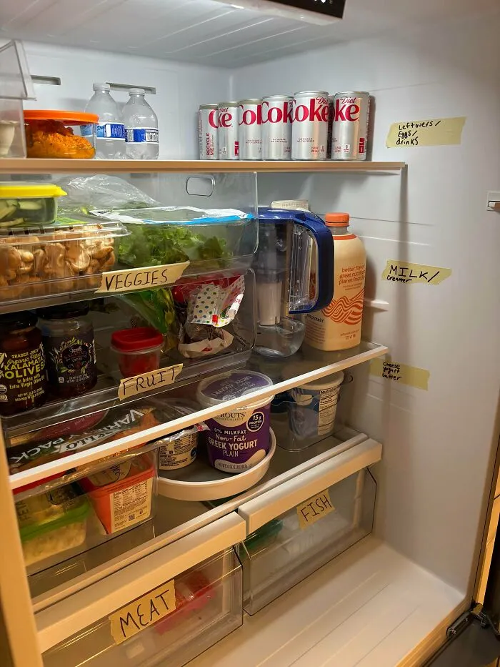 Organized fridge interior with labeled sections for veggies, fruit, meat, fish, milk, and drinks including Diet Coke cans.