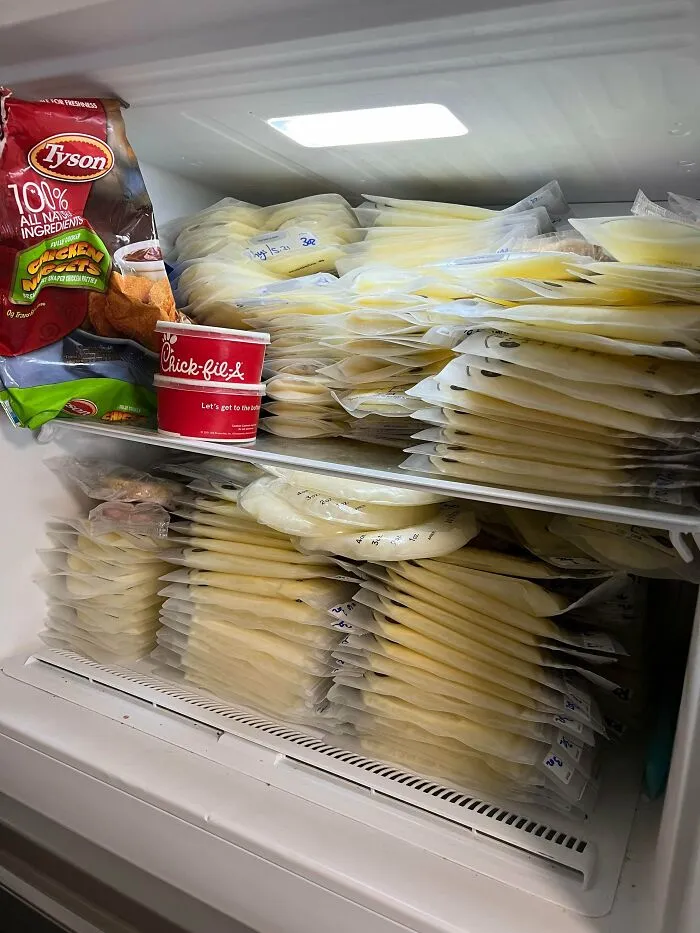 Stacked bags of frozen breast milk filling a fridge alongside frozen chicken nuggets and a Chick-fil-A cup.