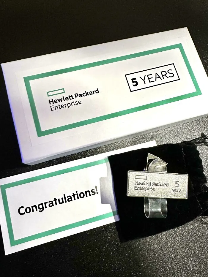 Hewlett Packard Enterprise 5 years pin and congratulations card on a black surface, U.S. warning concept image.
