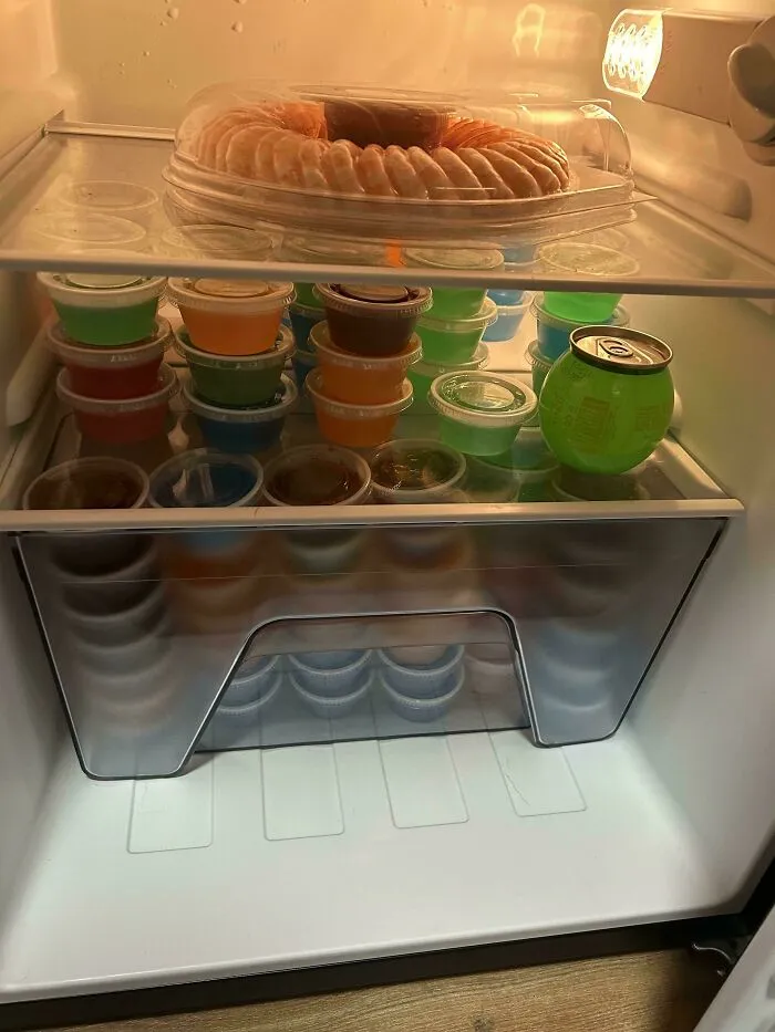 Opened fridge filled with neatly stacked colorful gelatin cups and a shrimp ring under fridge light, showing an unusual fridge finding.