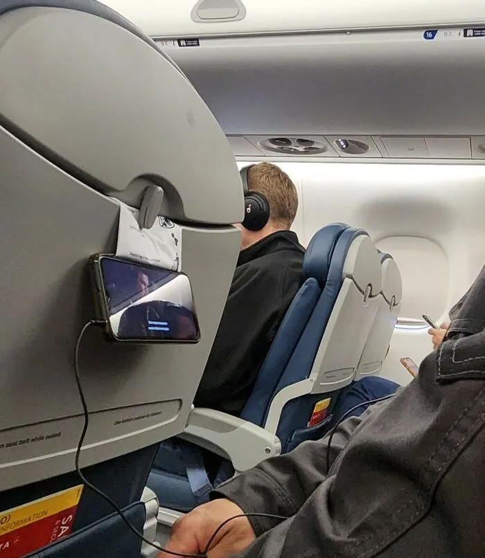 Airplane passenger using a phone holder hack stuck to the seat back showcasing a clever if it's stupid but it works example.