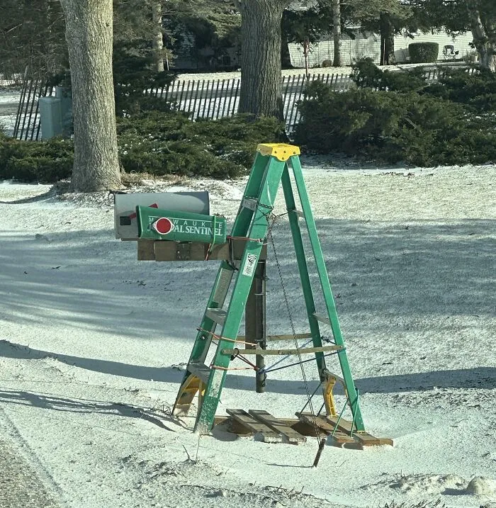 Green ladder repurposed as a mailbox stand secured with ropes on a snowy suburban lawn, an example of clever if it works design.