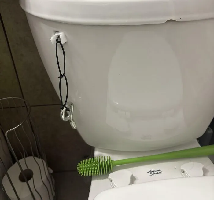 Toilet tank with a makeshift handle using elastic cords and a bolt as an example of if it's stupid but it works.