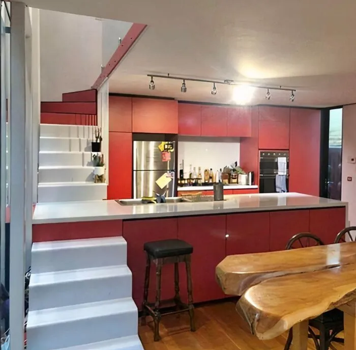 Modern kitchen featuring red cabinets, white stairs, and wooden dining table, an example of if it's stupid but it works design.
