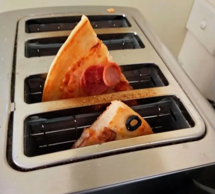 Two slices of pizza stuck upright in a toaster, showcasing a creative if it works then it's not stupid example.