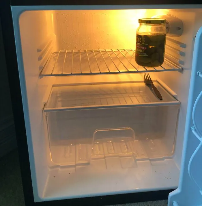 Nearly empty fridge with a jar of pickles and a lone fork, showing a surprising and horrifying fridge find.