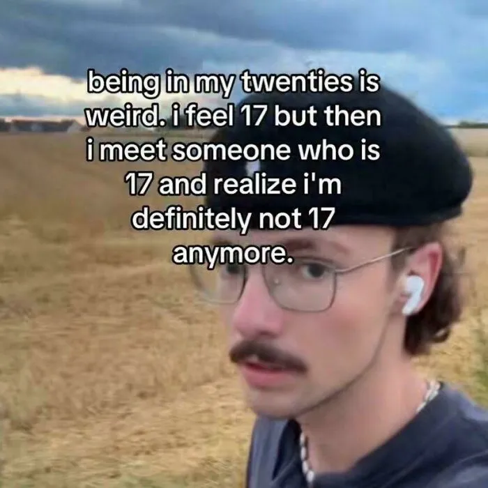 Young man with glasses and beret outdoors, relatable meme about feeling younger but realizing age difference, hilarious memes.