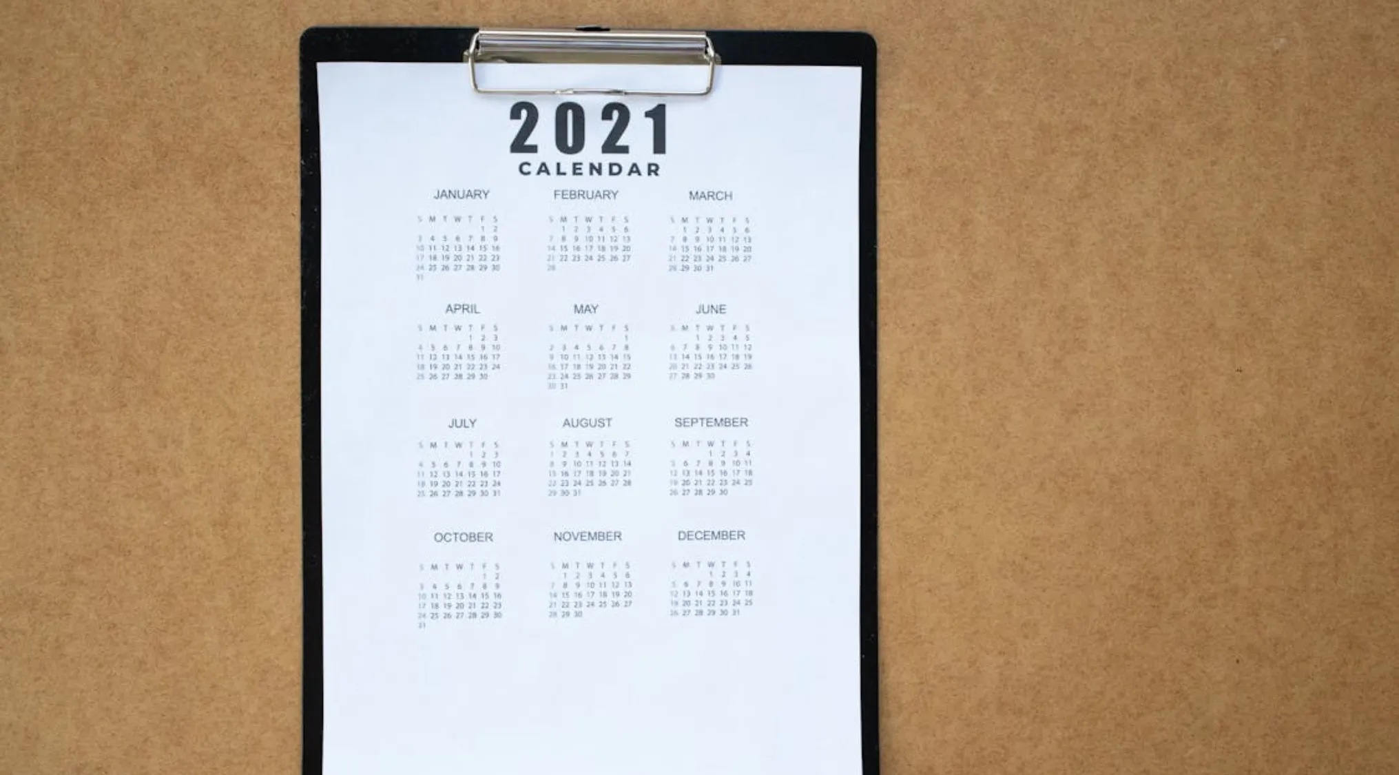 2021 calendar on clipboard on brown surface, illustrating basic math skills with days in 3 weeks concept.