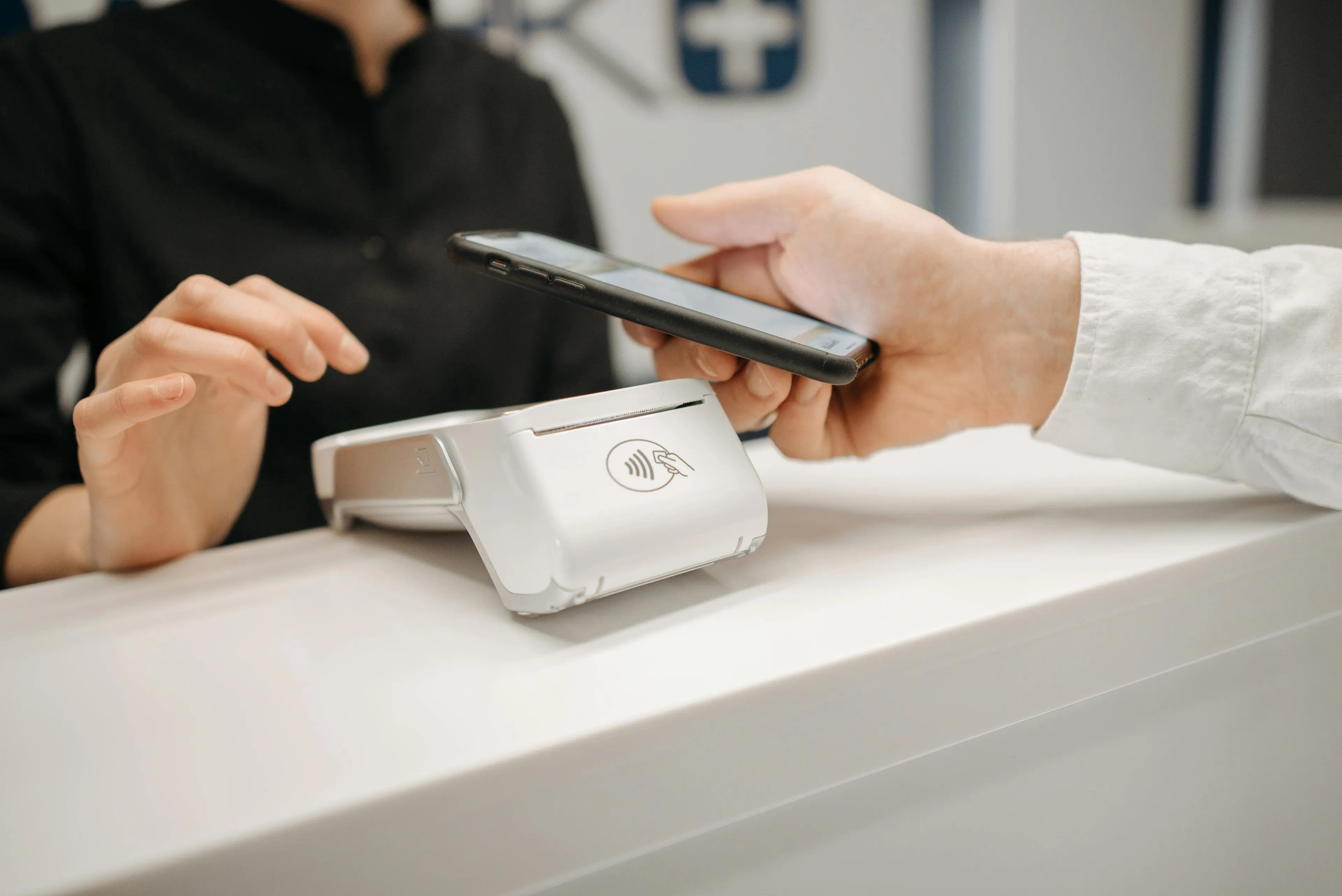Customer making a contactless payment with a smartphone using a mobile payment terminal at a modern checkout counter.