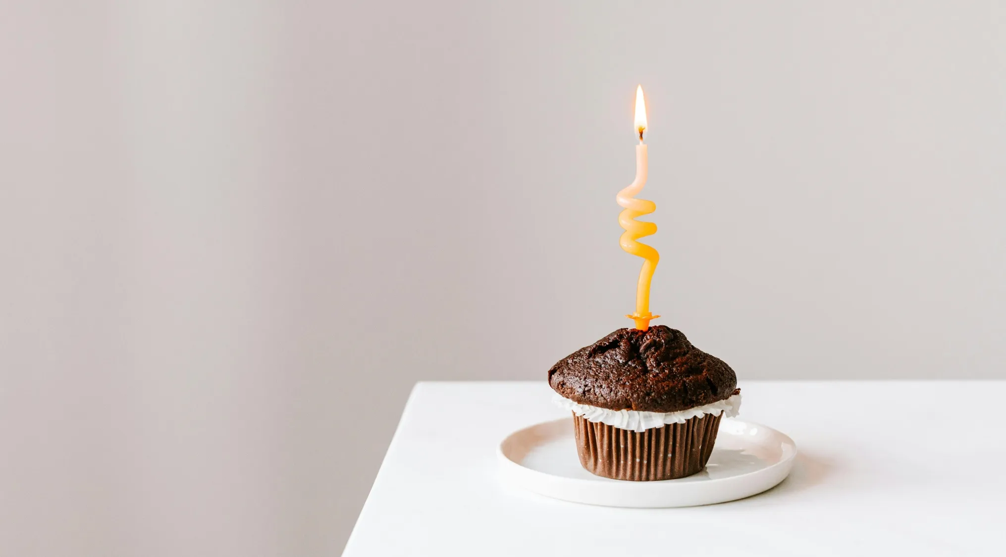 Chocolate cupcake on a white plate with a lit birthday candle for movie quiz anniversary edition celebration.