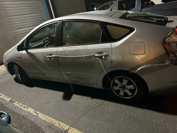 Silver car with door dent temporarily fixed using chains, demonstrating a clever example of if it’s stupid but it works then it’s not stupid.