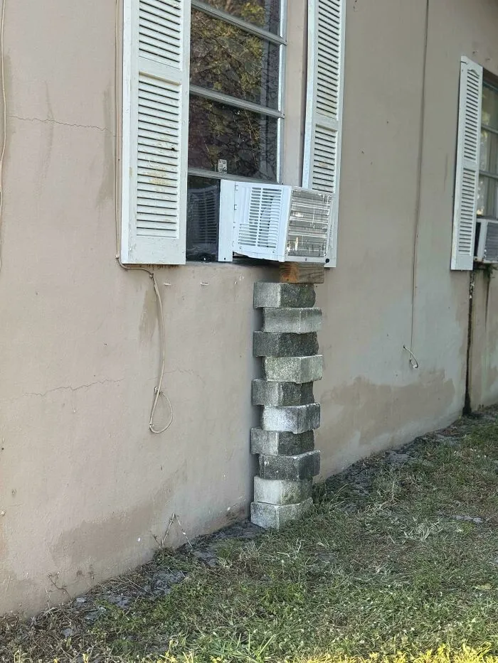 Air conditioner supported by stacked bricks in an example of if it's stupid but it works then it's not stupid.