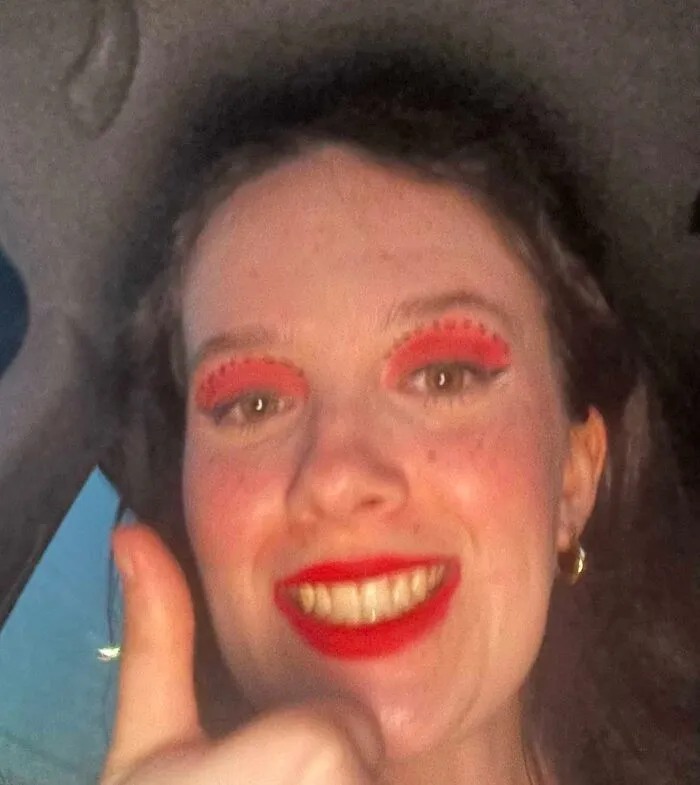 Person with bold red stage makeup smiling and giving thumbs up showcasing magical and mildly cursed stage makeup looks.
