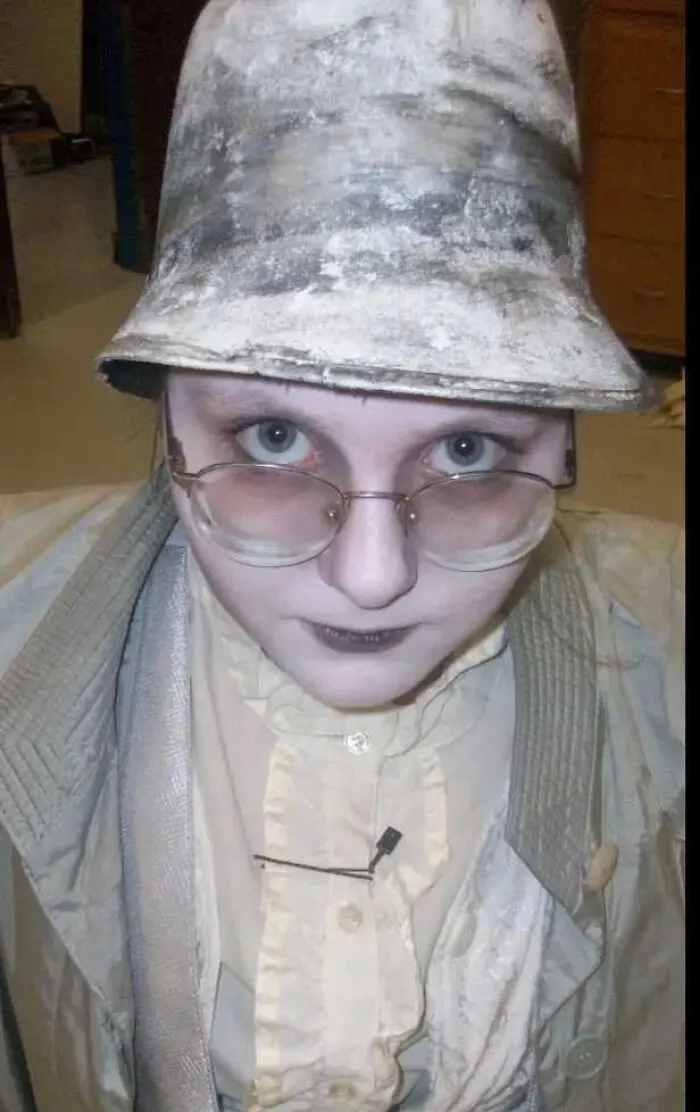 Person with stage makeup wearing a dirty bucket hat and glasses, showing a magical yet mildly cursed look on stage.