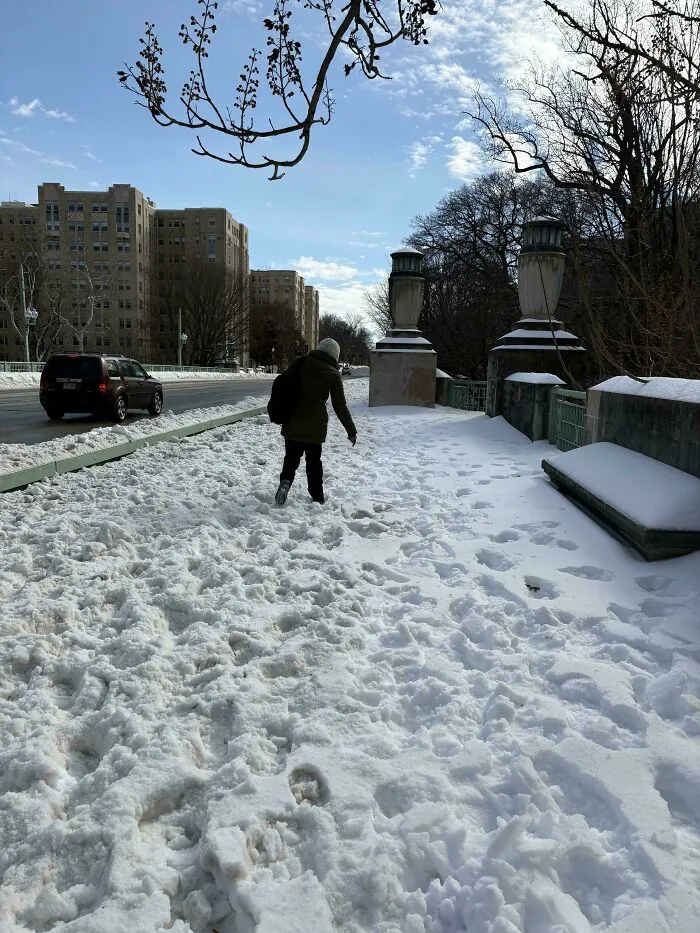 Person walking on a snow-covered sidewalk during a snowstorm hitting the U.S. with footprints in deep snow.