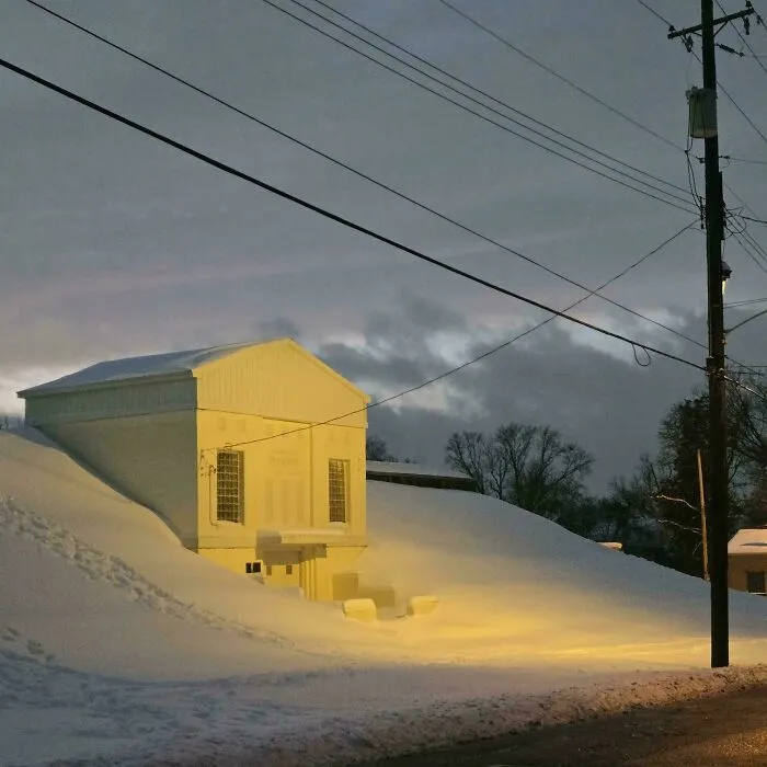 A snowstorm in the U.S. covers a building and street in deep snow under evening sky and streetlights.
