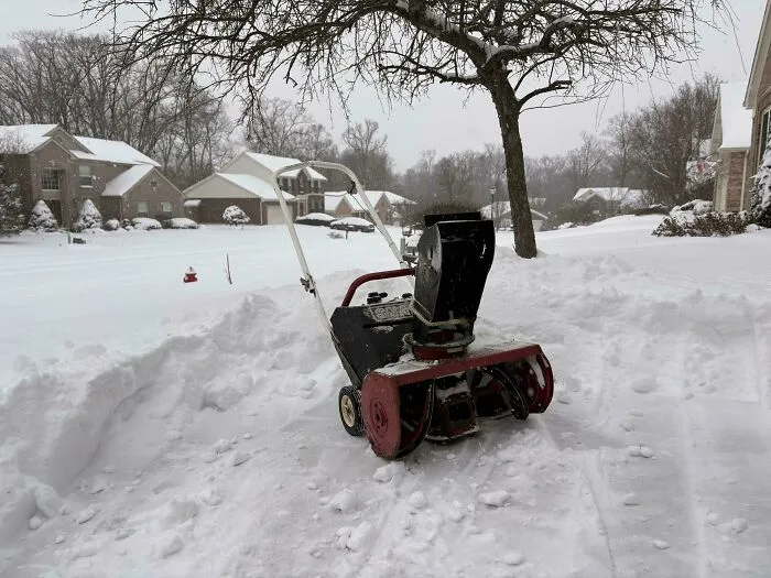Snowstorm in the U.S. with a snowblower clearing deep snow in a residential neighborhood covered in white.