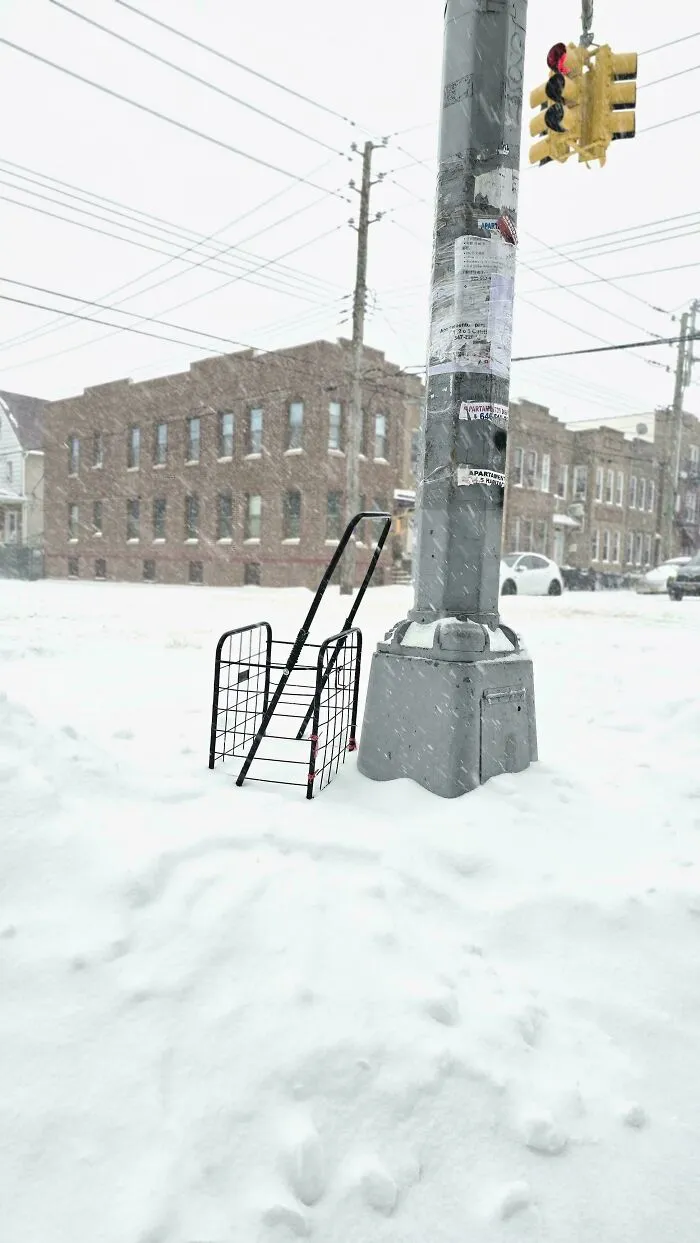 Snowstorm hitting a U.S. street with heavy snowfall covering the ground and a traffic light pole in an urban area.
