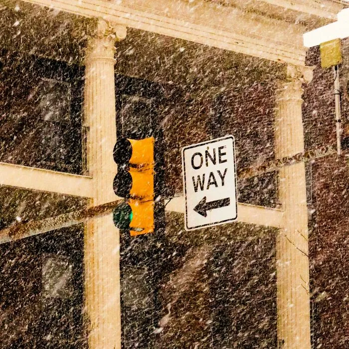 Traffic light and one way sign barely visible through heavy snowstorm hitting a U.S. city street during winter weather.