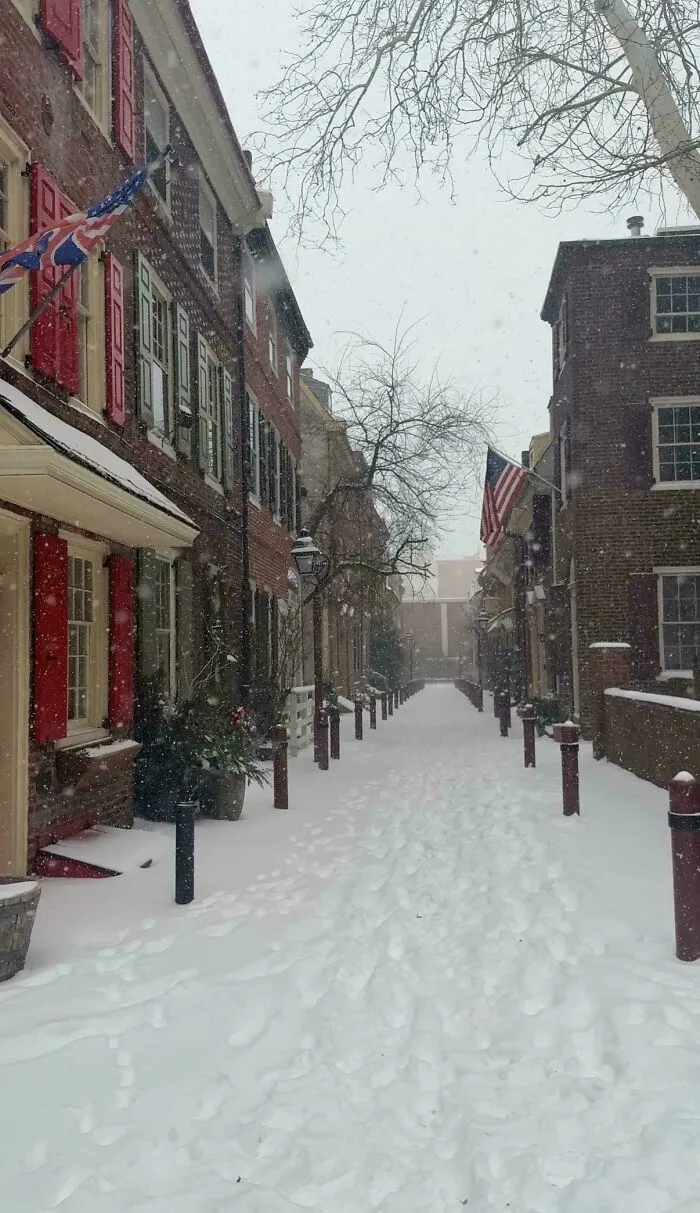 Snowstorm hitting a U.S. neighborhood street covered in snow with brick buildings and flags on a snowy winter day.