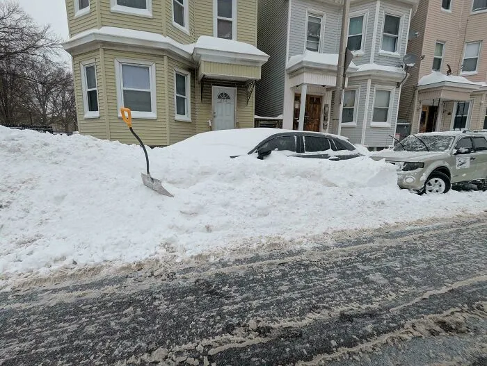 Snowstorm in the U.S. covering parked cars and streets with heavy snow and a shovel stuck in a snow pile.