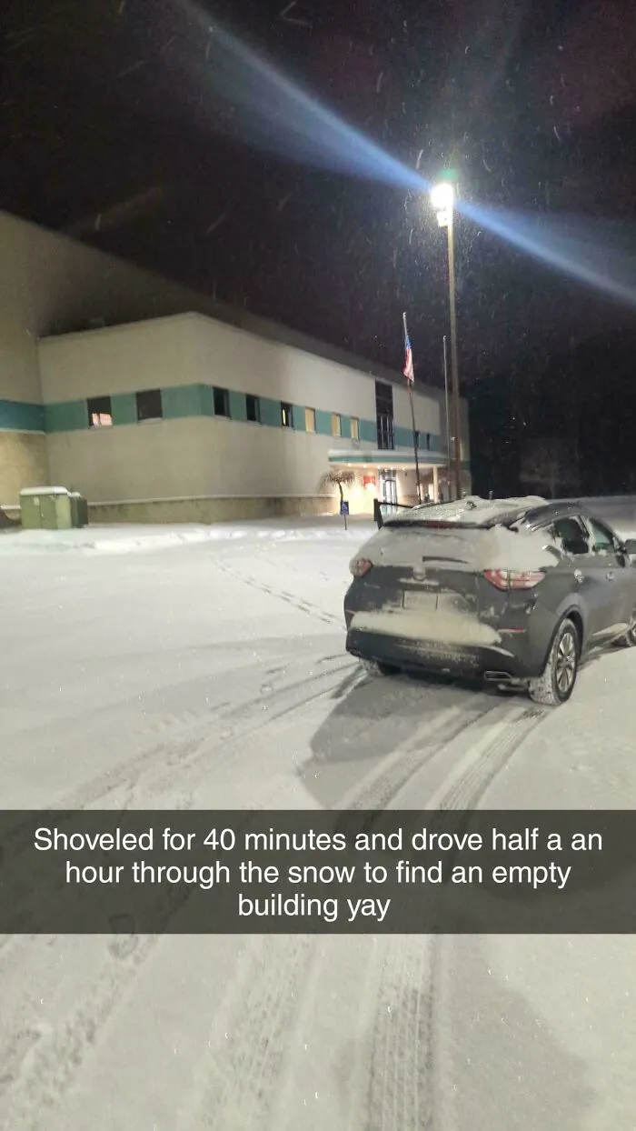 Car covered in snow parked outside a building at night during a snowstorm hitting the U.S. with fresh tire tracks in the snow.