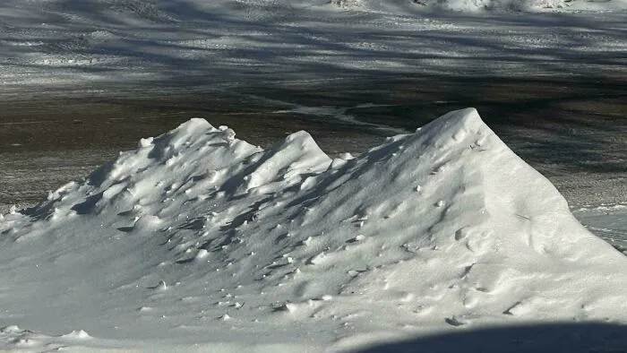 Snowstorm hitting the U.S. with snow piled into small drifts on a partially cleared road on a sunny day.