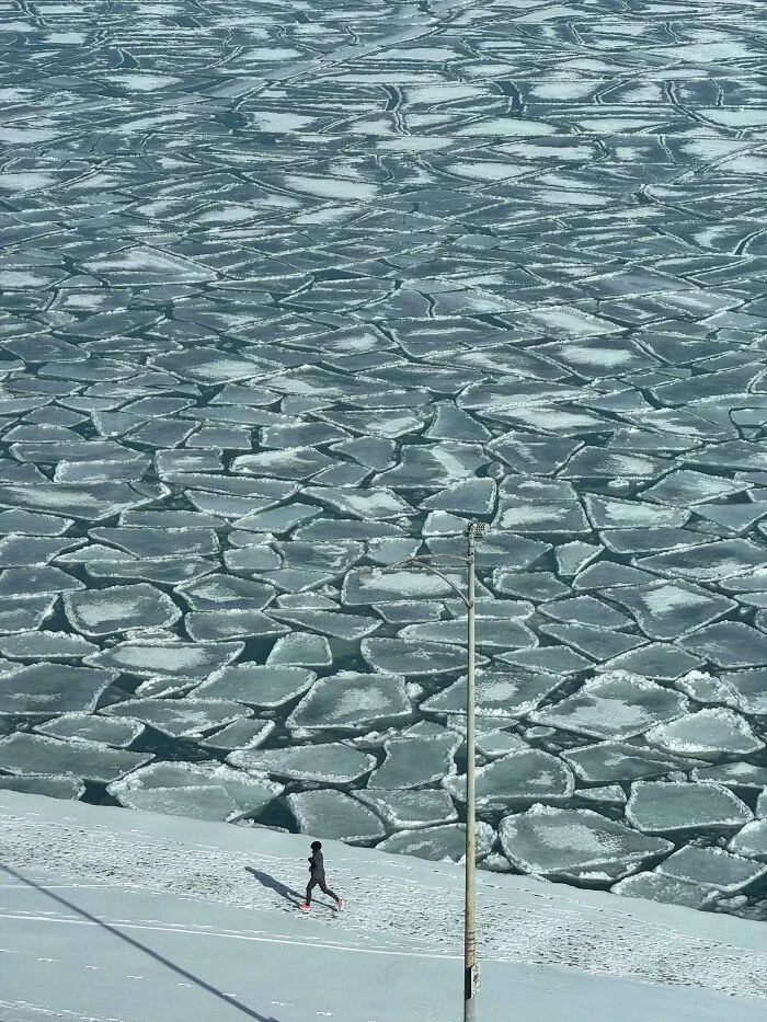 Person jogging on snow-covered ground near cracked ice on a frozen body of water during snowstorm in the U.S.
