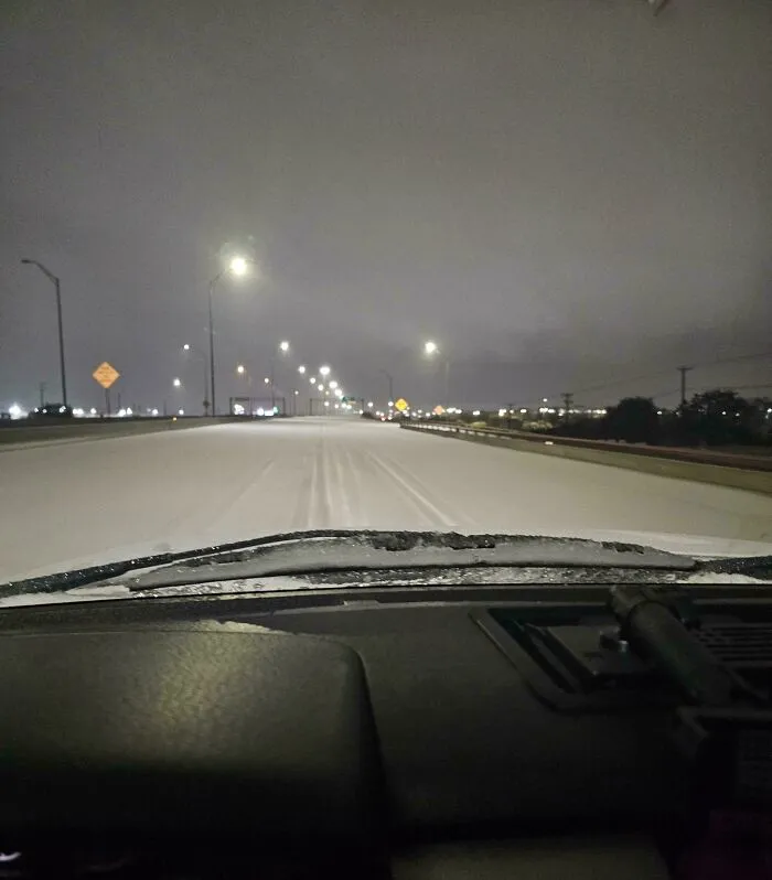 View from inside a car showing a snowstorm-covered highway in the U.S. under streetlights at night.