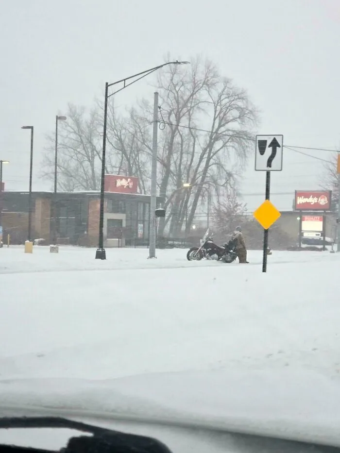 Snowstorm hitting the U.S. as a person struggles with a motorcycle in heavy snow near a Wendy's restaurant.