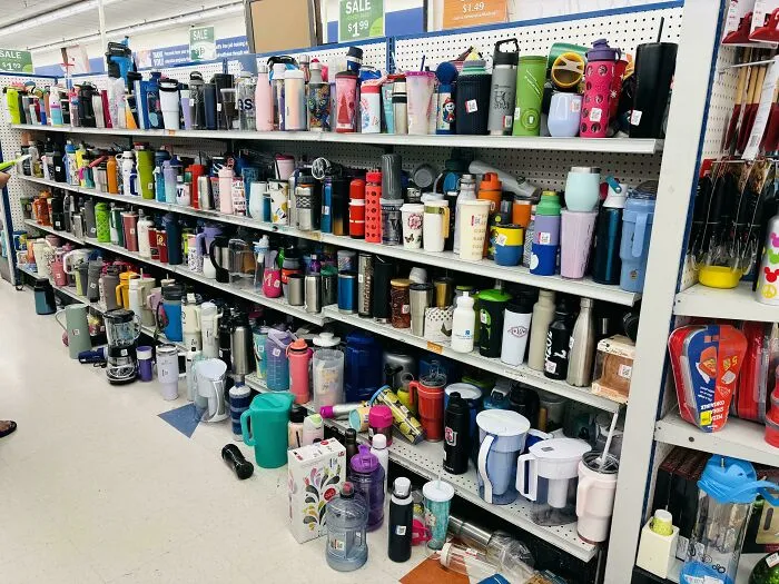 Shelves overflowing with reusable bottles and cups in a store, illustrating excess consumerism and clutter.