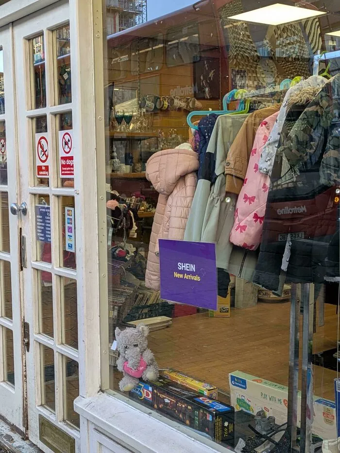 Store window display showing new clothing arrivals and toys, illustrating consumerism and distractions for the peasant class.